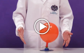 A mad science instructor standing behind a orange balloon on a desk