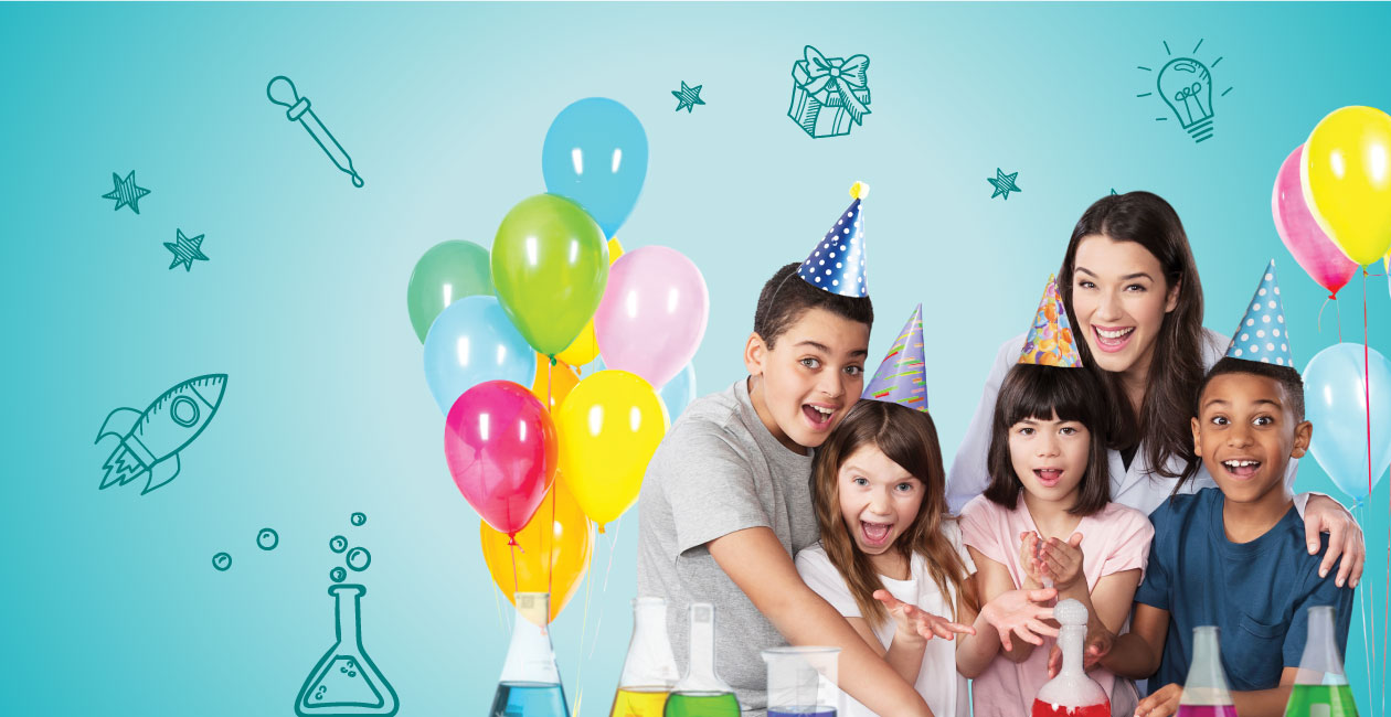 4 children smiling wearing party hats with their teacher behind them.  multi colored balloons next to them