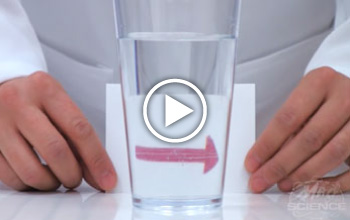 A mad Science instructor in front of a glass on the table. There is a play button imposed on the front of the image.