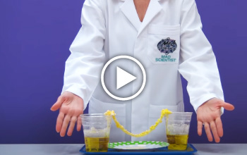 A mad science instructor presenting an experiment. There are two cups with a yellow liquid and a yellow rope is hanging from 